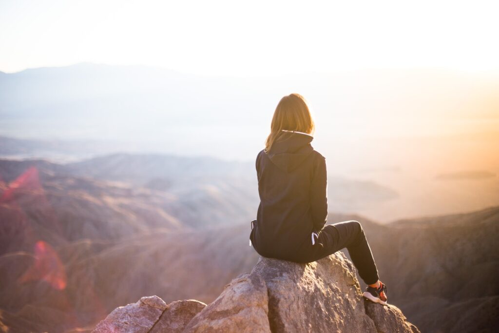 perfect sunlight balance - person sitting on top of gray rock overlooking mountain during daytime