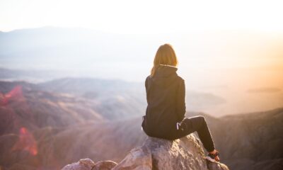 perfect sunlight balance - person sitting on top of gray rock overlooking mountain during daytime