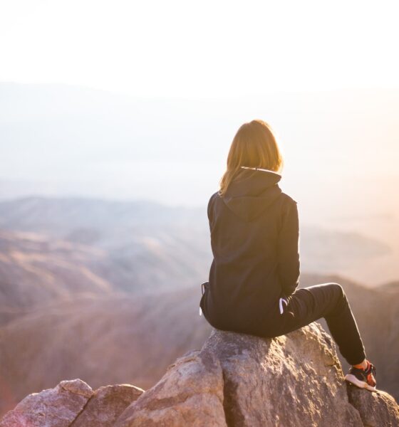 perfect sunlight balance - person sitting on top of gray rock overlooking mountain during daytime