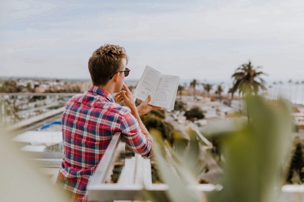 personal development - man reading book on balcony during daytim