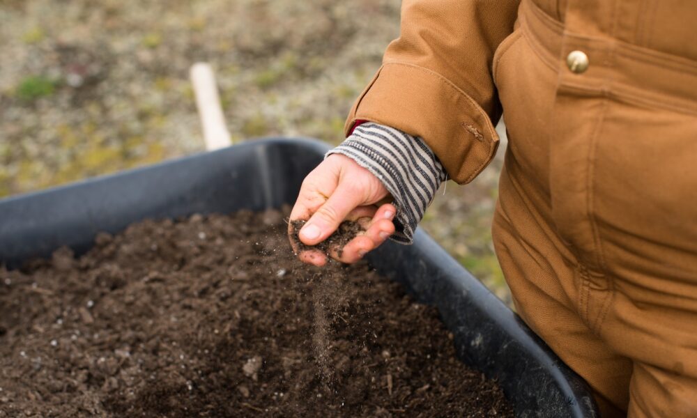 Soil Secrets - person in yellow jacket holding black soil